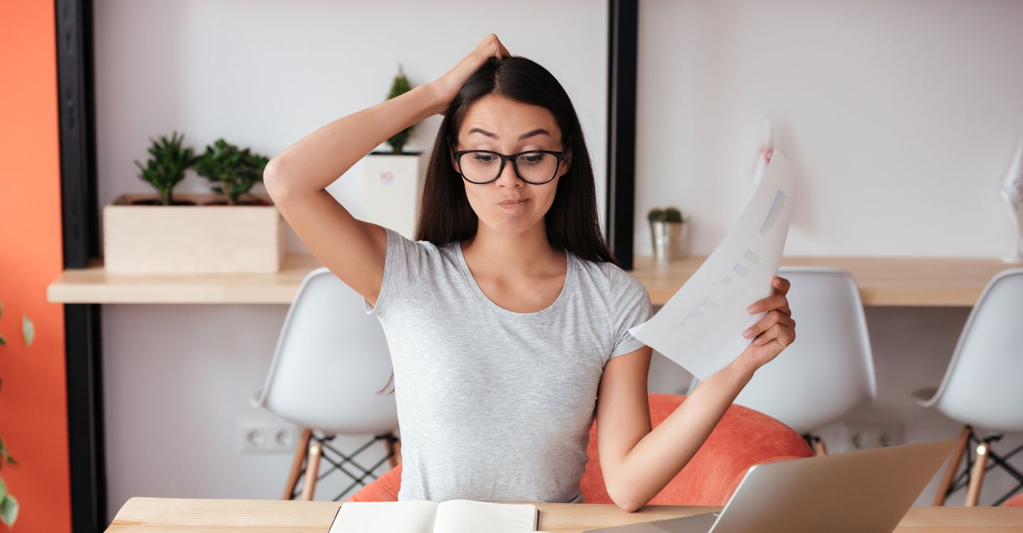 a woman looking at papers and a laptop confused